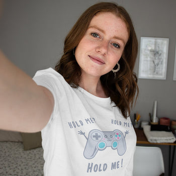 Woman wearing cute gaming tee of a game controller with adorable face, its arms stretching out, saying 'Hold Me? Hold Me!'.